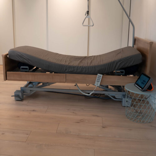 Pflegebett mit Matratze, bei der das Kopf- und das Fußende circa 25 cm angehoben sind. Auf weiteren Bildern ist das Produkt ohne Matratze zu sehen.