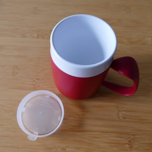 Doppelwandiger Kunststoffbecher, außen rot innen weiß mit transparentem Deckel.