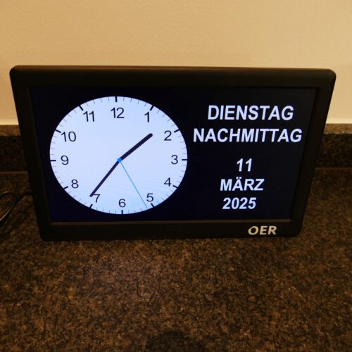 Selbststehender digitaler Bildschirm, der eine analoge Uhr, den Wochentag, vormittag/nachmittag und das Datum anzeigt.