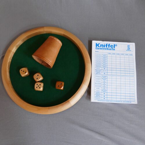 Dazu gehört eine runde Spielfläche, circa 25 cm Durchmesser, bespannt mit grünem Filz, 4 Würfel mit tastbaren Punkten, ein Würfelbecher und ein Block.