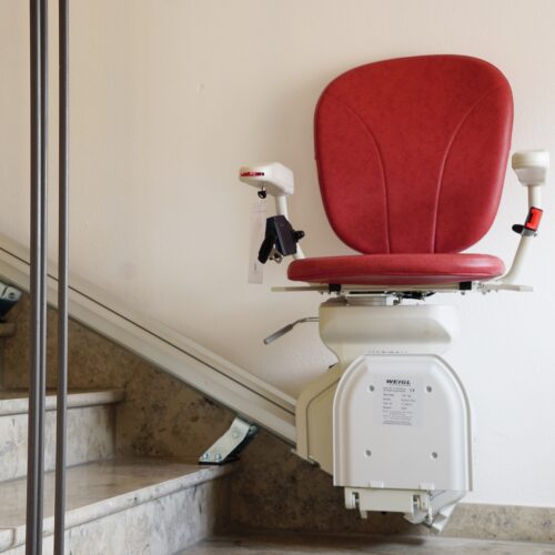 Treppenlift mit rotem Sitz, der auf Steintreppe befestigt ist.