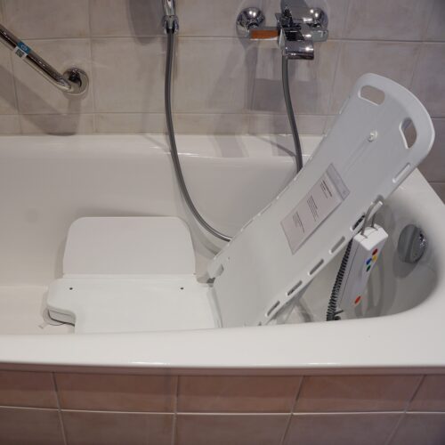Weißer Sitz in Badewanne mit Rückenlehne und Seitenflügeln. Wird zum Ein- und Aussteigen mit Fernbedienung hochgefahren.
