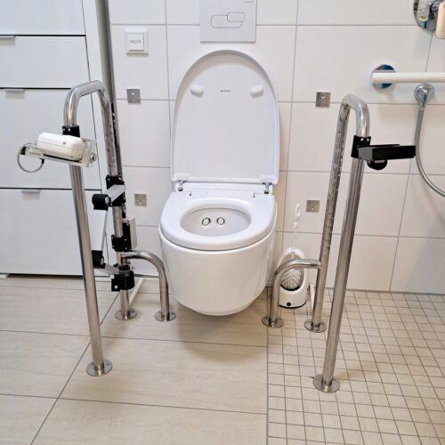 Toilette mit am Boden befestigten, seitlich abgestützten Haltebügeln. Insgesamt eine Vielzahl von Haltemöglichkeiten.