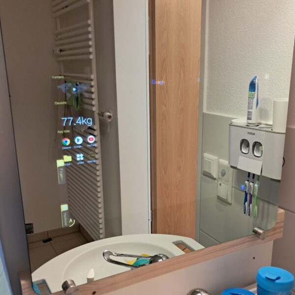 Ein Spiegel spiegelt das Badezimmer. Der Touchscreen mit seinen verschiedenen Anzeigen ist schwach zu sehen.