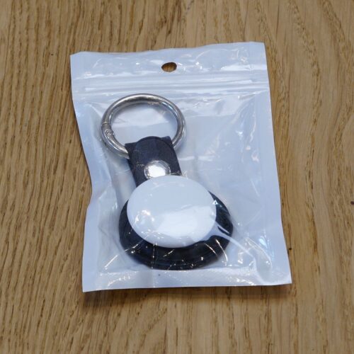 In Verpackung mit Klarsicht-Vorderseite ist ein Schlüsselanhänger mit Ring, an der anderen Seite rund, schwarz, mit 30 mm Durchmesser, weiße Fläche oben.