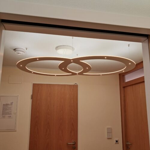 Besteht aus zwei abgehängten Ringen, mit circa 60 cm Durchmesser, die sich ein Stück überlappen. Das Licht kommt aus der circa 1 cm hohen Kante des Objekts