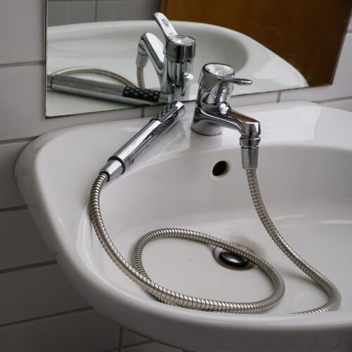 Im weißen Waschbecken liegt der Schlauch der Brause. Am Ende des Schlauchs ist der Brausenkopf, Stab, cirka 25 cm lang, mit den unterschiedlichen Düsen.