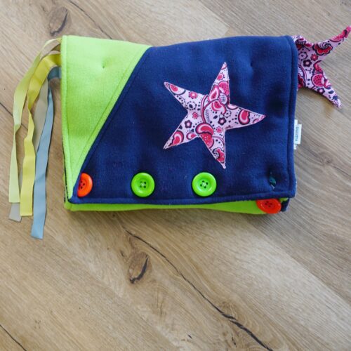 BlauGrüne Stofftasche mit bunten Knöpfen, Schnüren und weiteren Elementen zum Greifen und Fühlen.