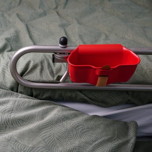 Rote Box, circa 18 cm lang, 7 cm tief, die mit Klettband an das Seitenteil des Pflegebettes befestigt wird