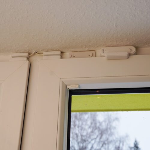 Am oberen Rahmen des Fensterflügels ist ein Teil des Sensors (cirka 5 cm lang und 2 cm hoch, weiß) befestigt. Das Gegenstück ist darüber am Fensterstock befestigt.