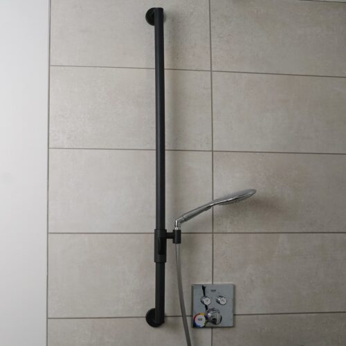 Vor den hellbeigen Fliesen hängt senkrecht die dunkelgraue 110 cm lange Brause-Haltestange mit dem magnetischen Duschkopfhalter